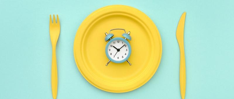 Alarm clock on yellow plate with cutlery against a blue background