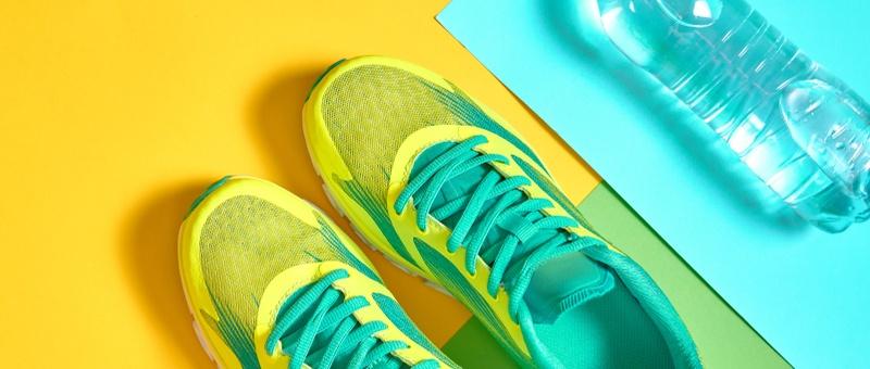 Yellow and turquoise trainers against yellow and green backdrop beside plastic water bottle resting on blue paper.