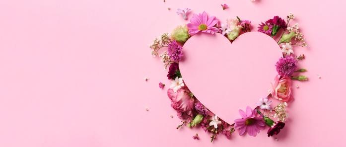 Pink heart on pink background surrounded by red, white and pink flowers.