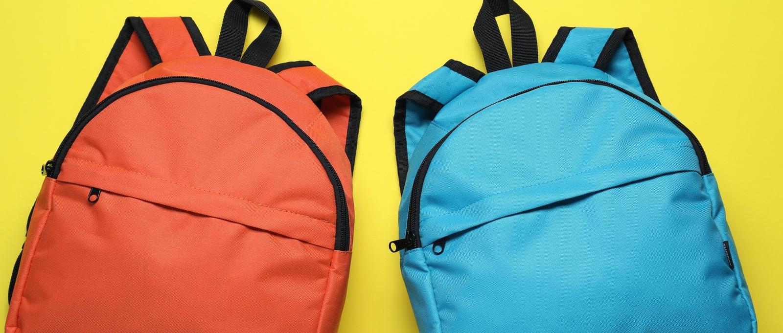 Stylish orange and blue backpacks on yellow background