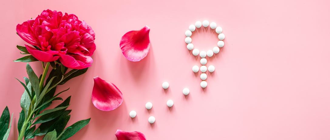 Gender Venus symbol made of pills, and peony flower petals on a pink background, woman period and health concept.