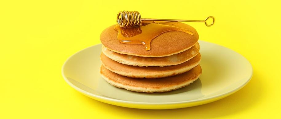 Plate of tasty pancakes with honey on colour background
