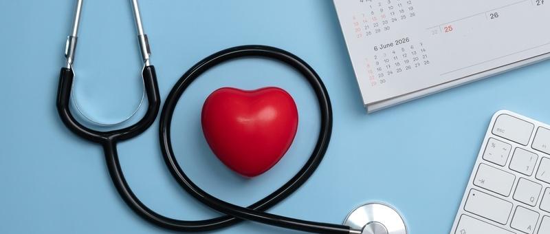 Stethoscope, red heart, calendar and white computer keyboard against blue background.