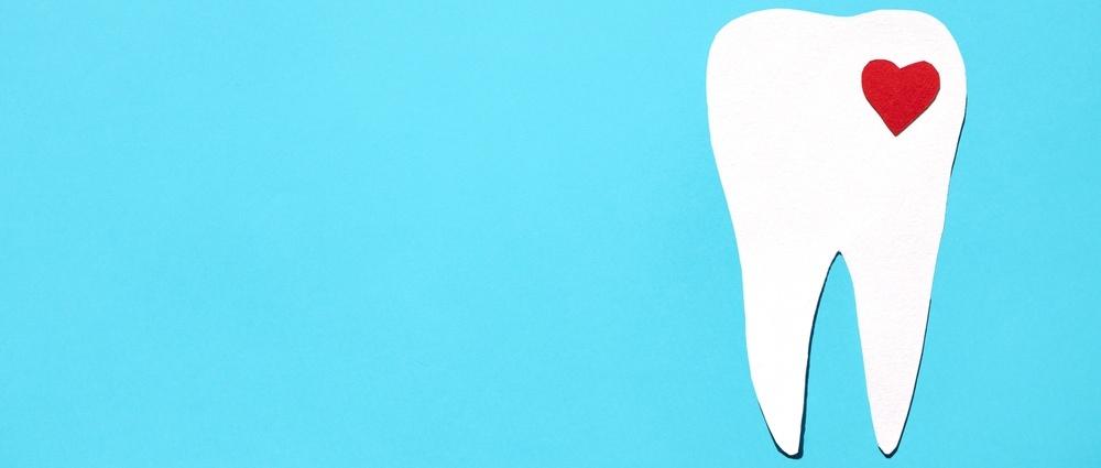Silhouette of a tooth with a red heart on a blue background. Dental health concept. Flat lay, place for text.