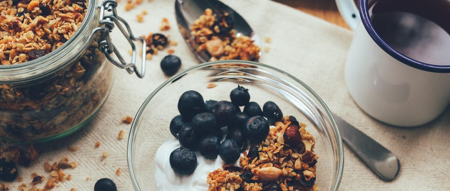 Fresh blueberries and homemade granola in a glass bowl with yoghurt, alongside a storage jar of granola.