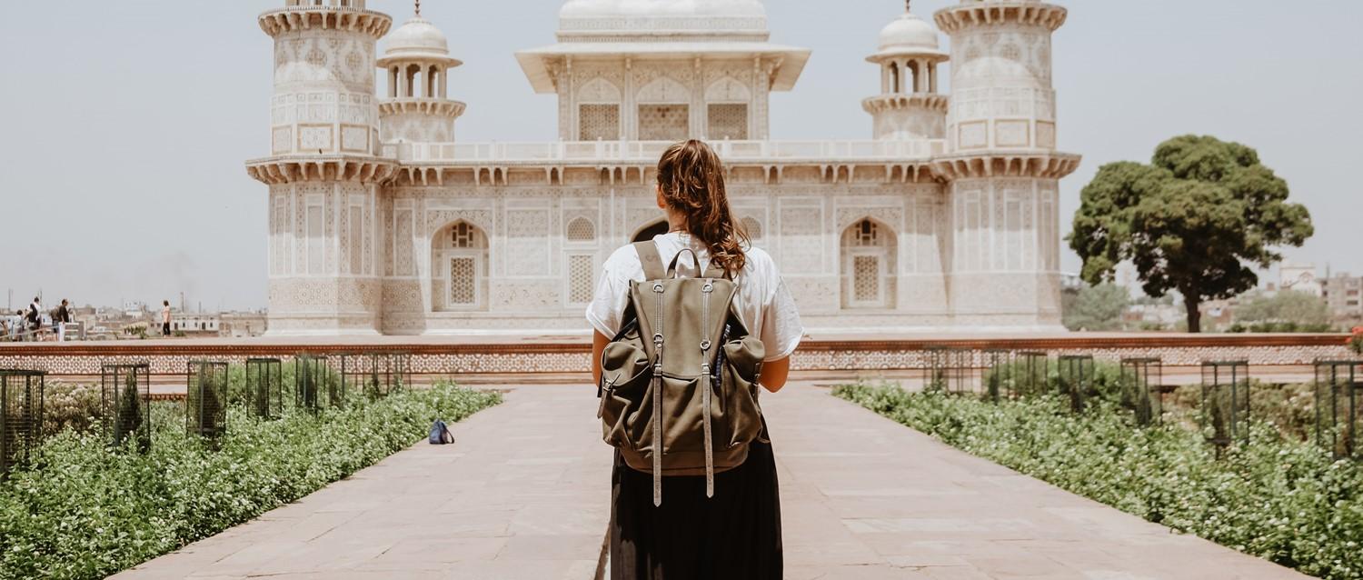 Traveller with backpack admiring ornate white marble mausoleum in India, likely Baby Taj, on sunny day.