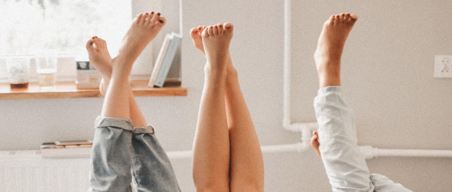 Three pairs of bare feet raised in the air against a bright bathroom wall, with a bathtub visible in the foreground.